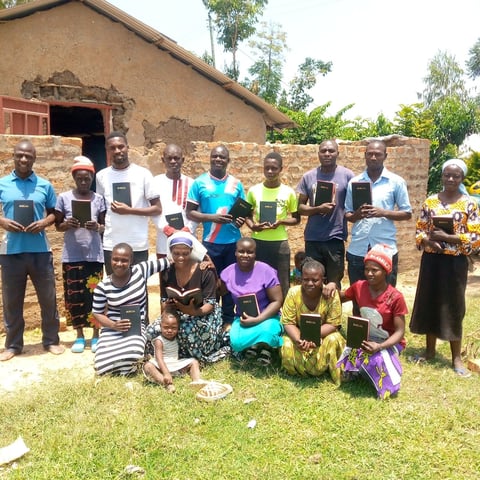 Group of African men, women, and children holding mobile devices standing and sitting in front of a brick building
