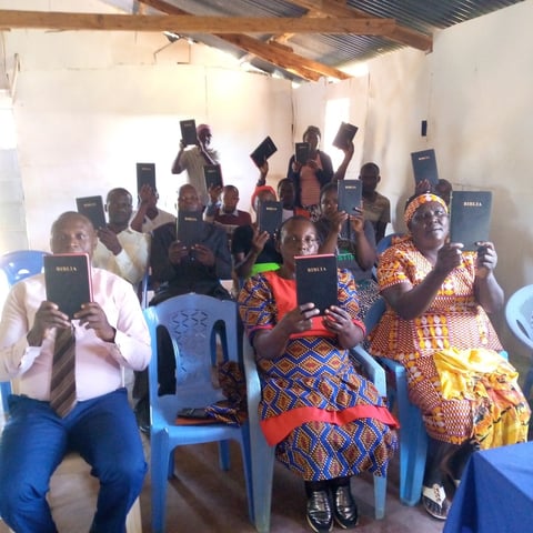 Group of people holding Bibles in an indoor community gathering or religious meeting in a modest concrete room