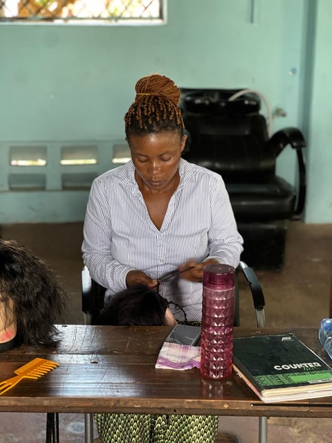 Woman in striped shirt writing or taking notes at a wooden desk in an indoor room with turquoise walls