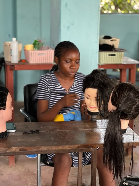 Woman in striped shirt working with mannequin heads at a table in a beauty salon setting with light blue walls